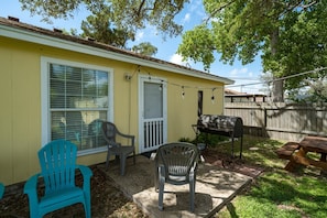 A backyard with a barbecue grill, two plastic chairs, a picnic table, and a wooden fence. - Coastal Soul by Miss Kitty’s (Aransas Pass)