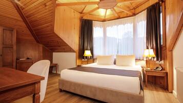 Ein gemütliches Schlafzimmer im Holzstil mit einem großen Bett, zwei Nachttischen mit Lampen, einem Schreibtisch und einem Sessel.