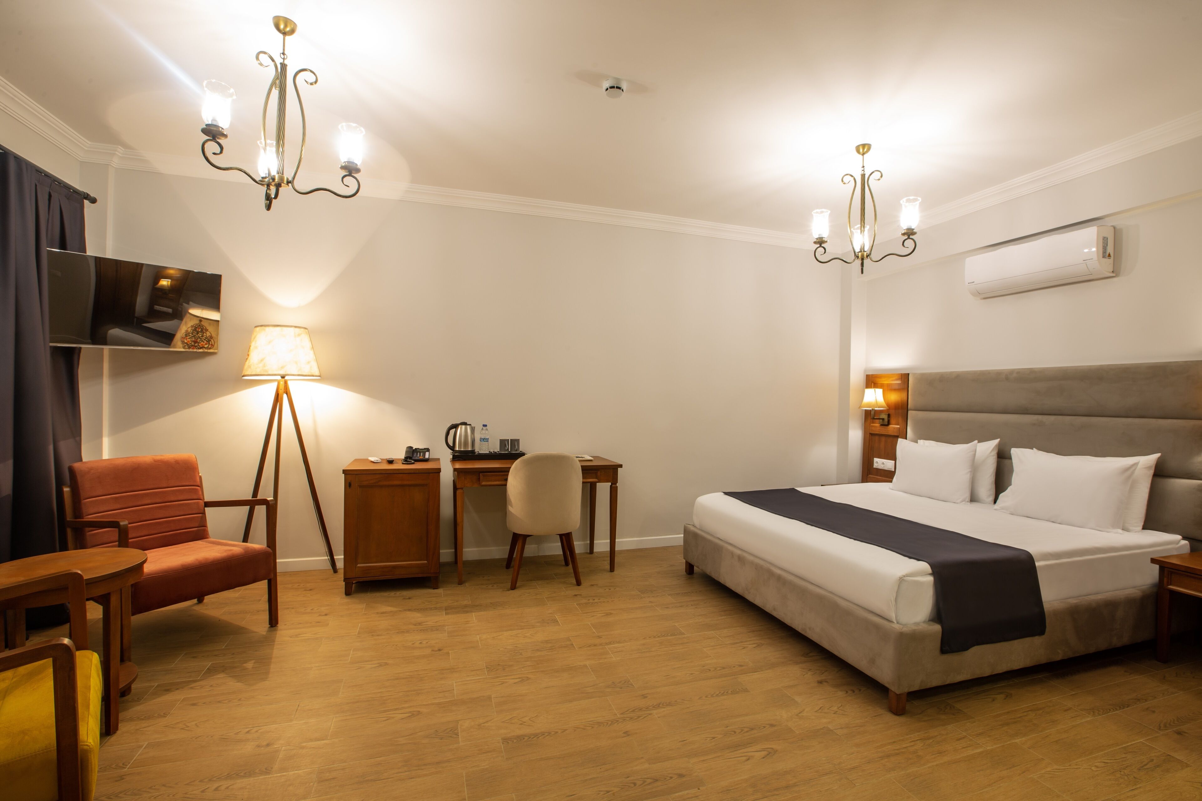 A hotel room with a bed, desk, chair, and two chandeliers.