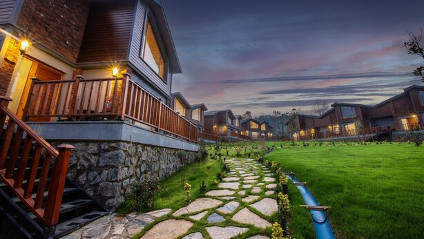 Um complexo residencial moderno com caminhos de pedra, guarda-corpos de madeira e várias casas com janelas iluminadas.