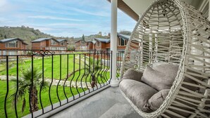 Uma varanda com uma cadeira suspensa, vista para casas e um gramado bem cuidado.