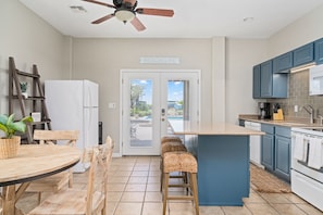 Enjoy cooking in this kitchen with a central island, bar stools, microwave, and dishwasher, plus a ceiling fan and backyard view.