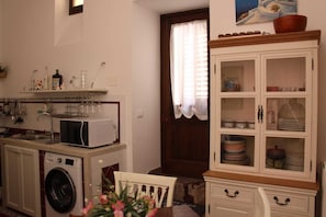 A compact kitchen with a washing machine, a microwave, and a cabinet with dishes.
