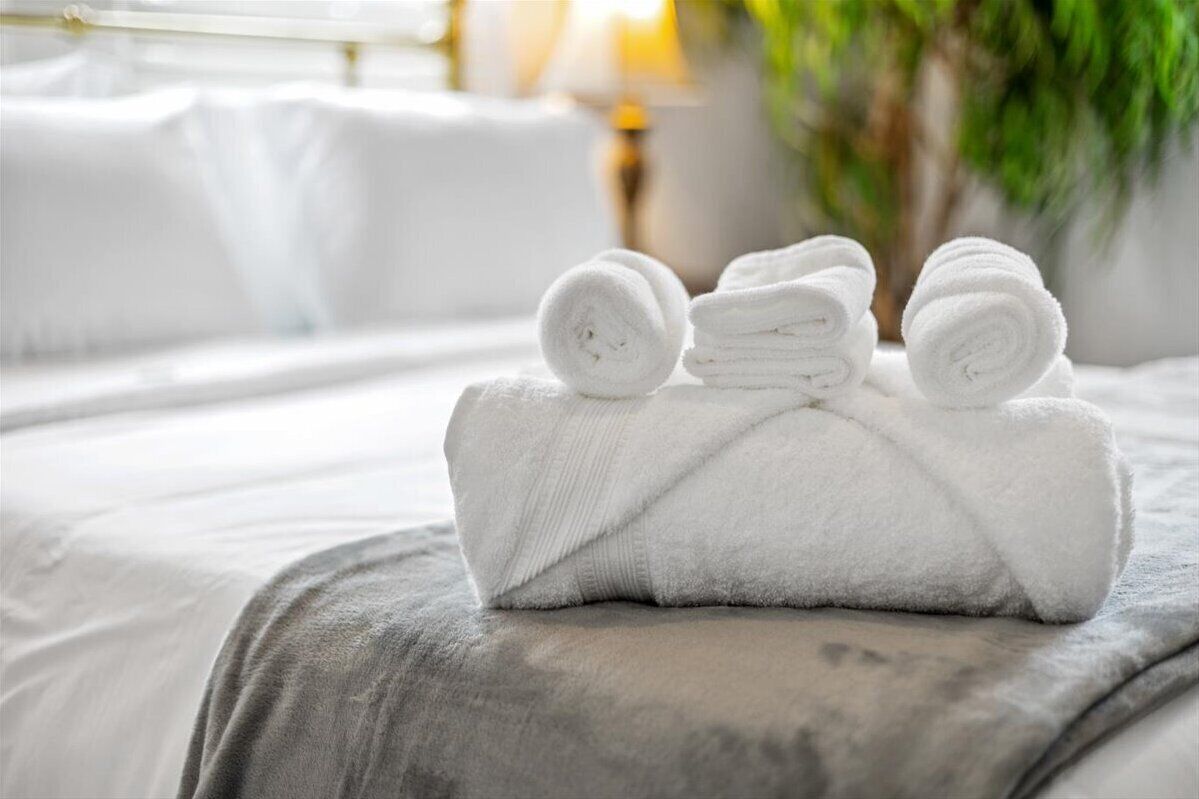 A neatly made bed with rolled white towels and a grey blanket.