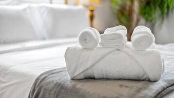 A neatly made bed with rolled white towels and a grey blanket.