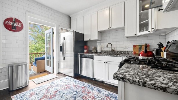 A modern kitchen with white cabinets, a stainless steel refrigerator, a dishwasher, and a granite countertop. - Historic Retreat in Lake Claire (Atlanta)