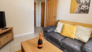 A living room with a grey sofa, a wooden coffee table with a bottle of Canti Prosecco, a television, and a painting of a bull on the wall. - Hafan Fach (Mold)