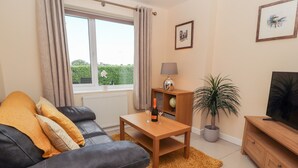 A living room with a sofa, a wooden coffee table, a TV stand, a lamp, and a potted plant. - Hafan Fach (Mold)