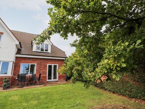 A two-story house with a brick facade, a tiled roof, and a small patio with outdoor furniture. - Hafan Fach (Mold)