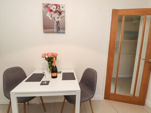 A dining table with two chairs, a vase with flowers, a bottle of Canti champagne, and two glasses. - Hafan Fach (Mold)