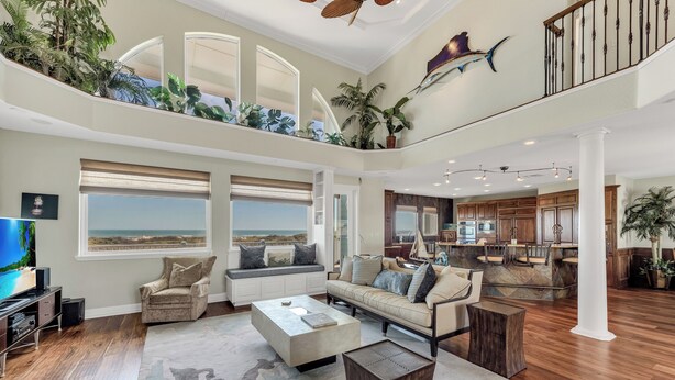 A spacious living area with a large window overlooking the ocean, a cozy seating area, and a kitchen with wooden cabinets.