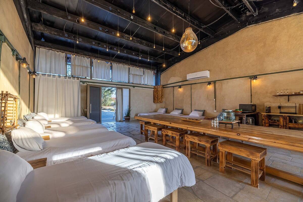 A spacious room with multiple beds, a long wooden table, and a bar area.