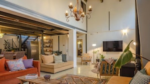 A spacious living room with a sofa, armchairs, a coffee table, and a patterned rug. A television is mounted on the wall, and a chandelier hangs from the ceiling. - ibex unique Desert Inn (Ramat Negev)