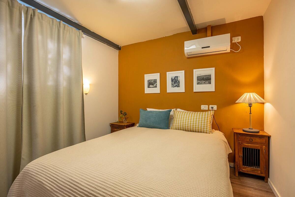 A bedroom with a bed, a nightstand, a lamp, and an air conditioning unit.