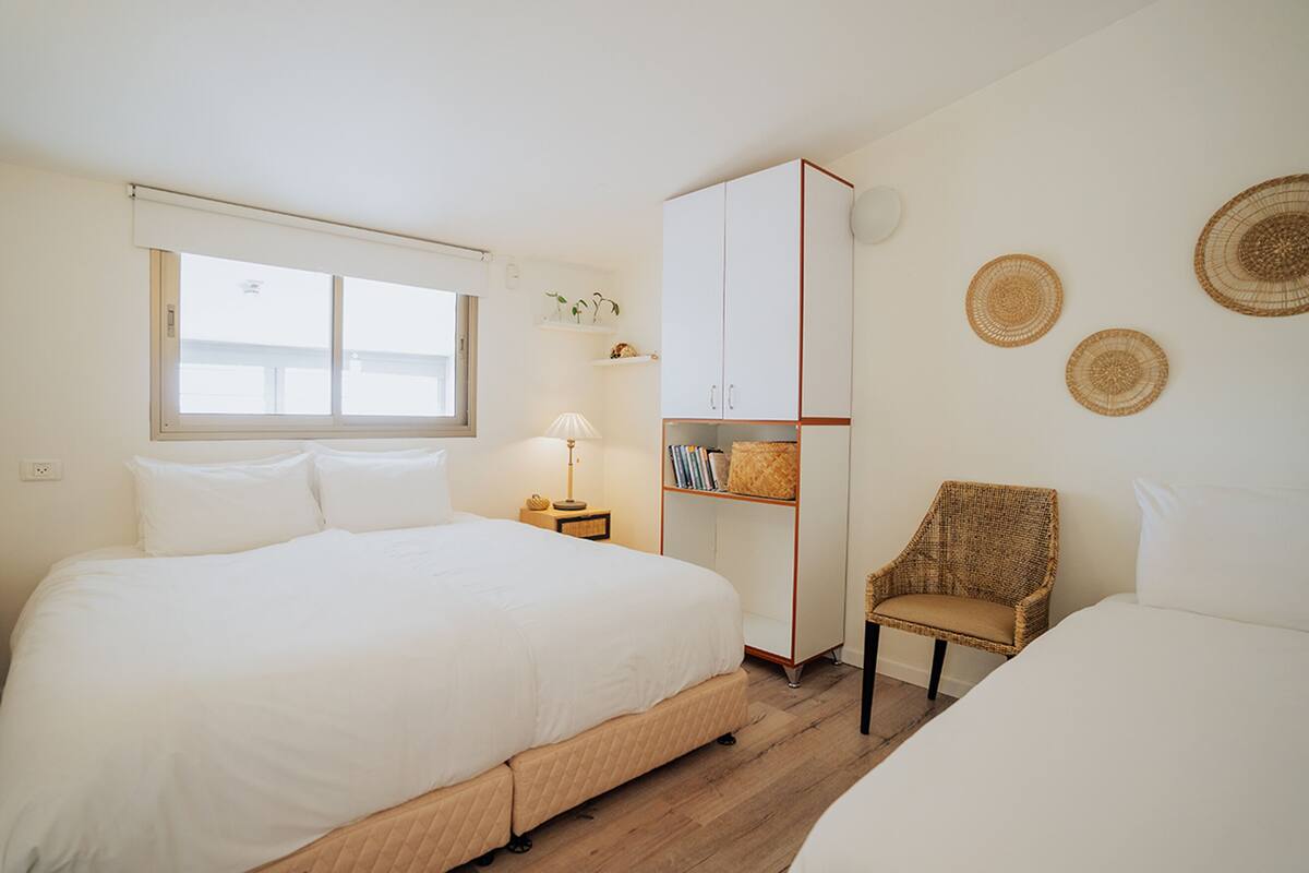 A bedroom with a large bed, a nightstand with a lamp, a wicker chair, and a wardrobe.