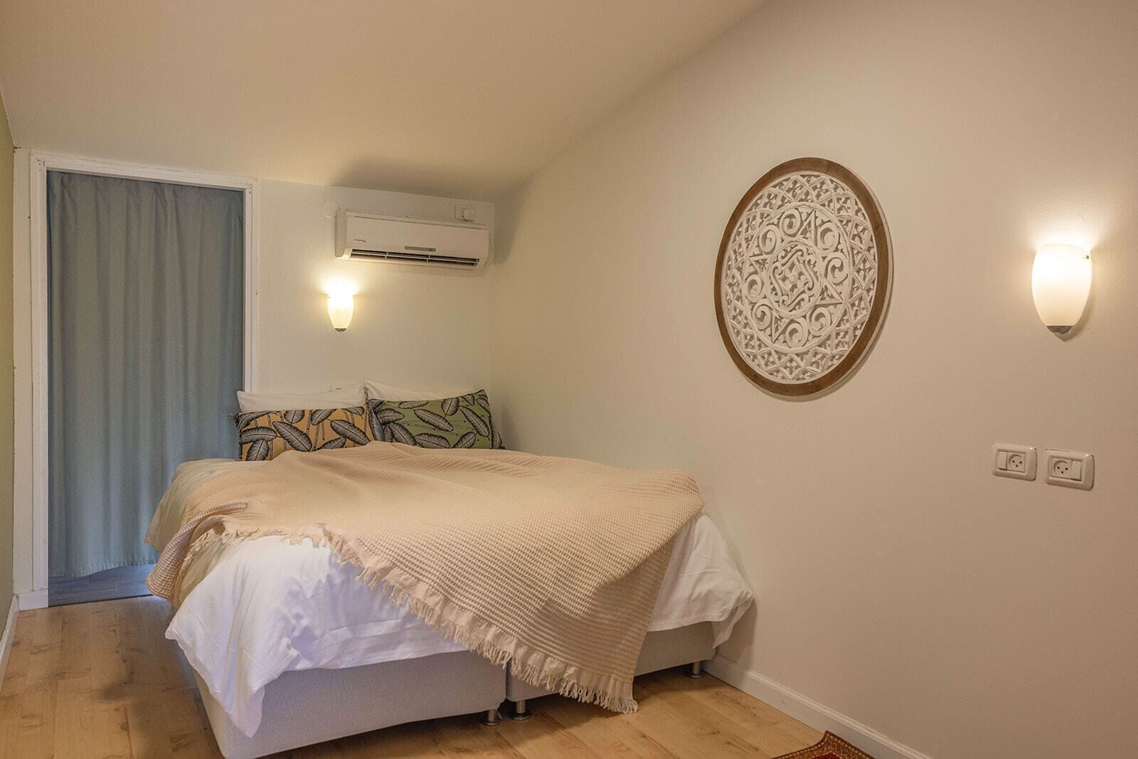 A bedroom with a bed, an air conditioner, a decorative wall piece, and a light fixture.