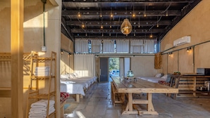 A rustic room with multiple beds, a long wooden table, and shelves with towels. - ibex unique Desert Inn (Ramat Negev)