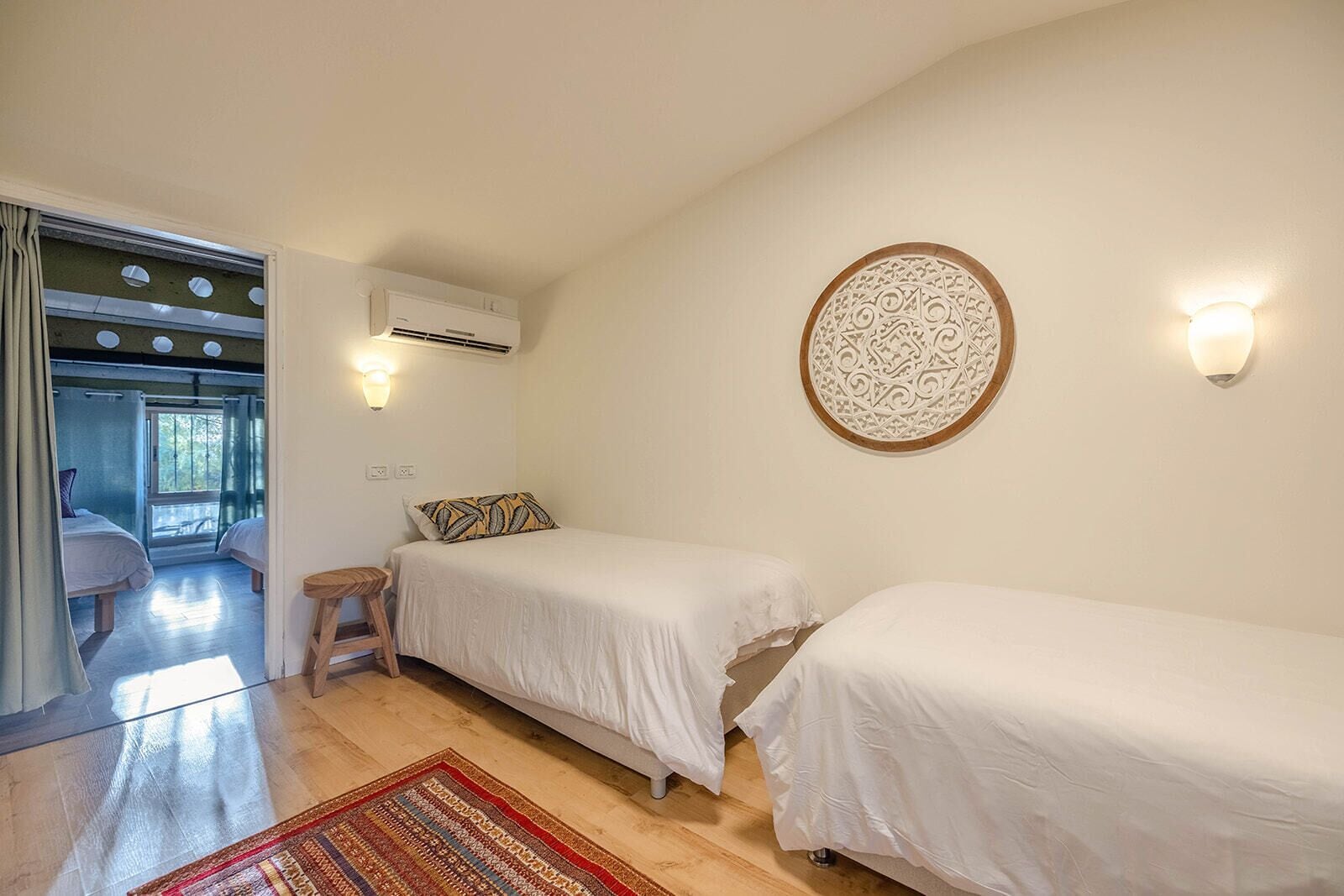 Un dormitorio con dos camas, piso de madera, alfombra estampada y un adorno de pared.