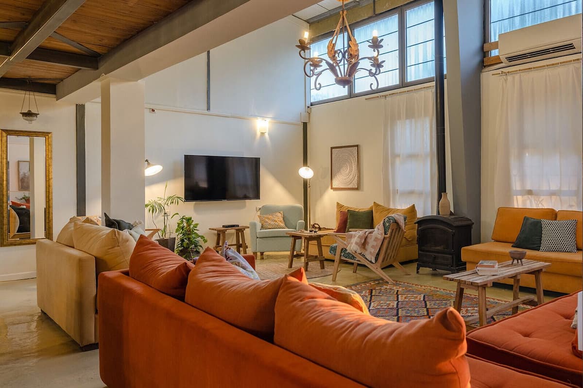 A spacious living room with a large sofa, a wooden coffee table, a fireplace, and a television mounted on the wall.