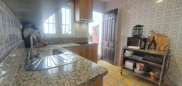 Una cocina con encimeras de granito, un lavamanos de acero inoxidable, una puerta de madera y un estante con utensilios de cocina.