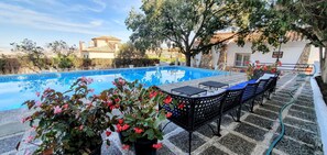 Una piscina con borde de baldosas, rodeada de plantas en macetas y mobiliario de exterior.