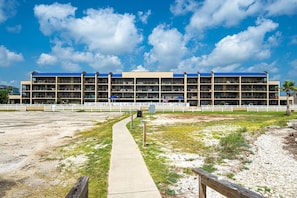 A multi-story building with a central courtyard, a pathway leading to the entrance, and a white fence surrounding the property. - Laguna Reef 308 - Beautiful Bay View by Ryson Vacation Rentals (Rockport)