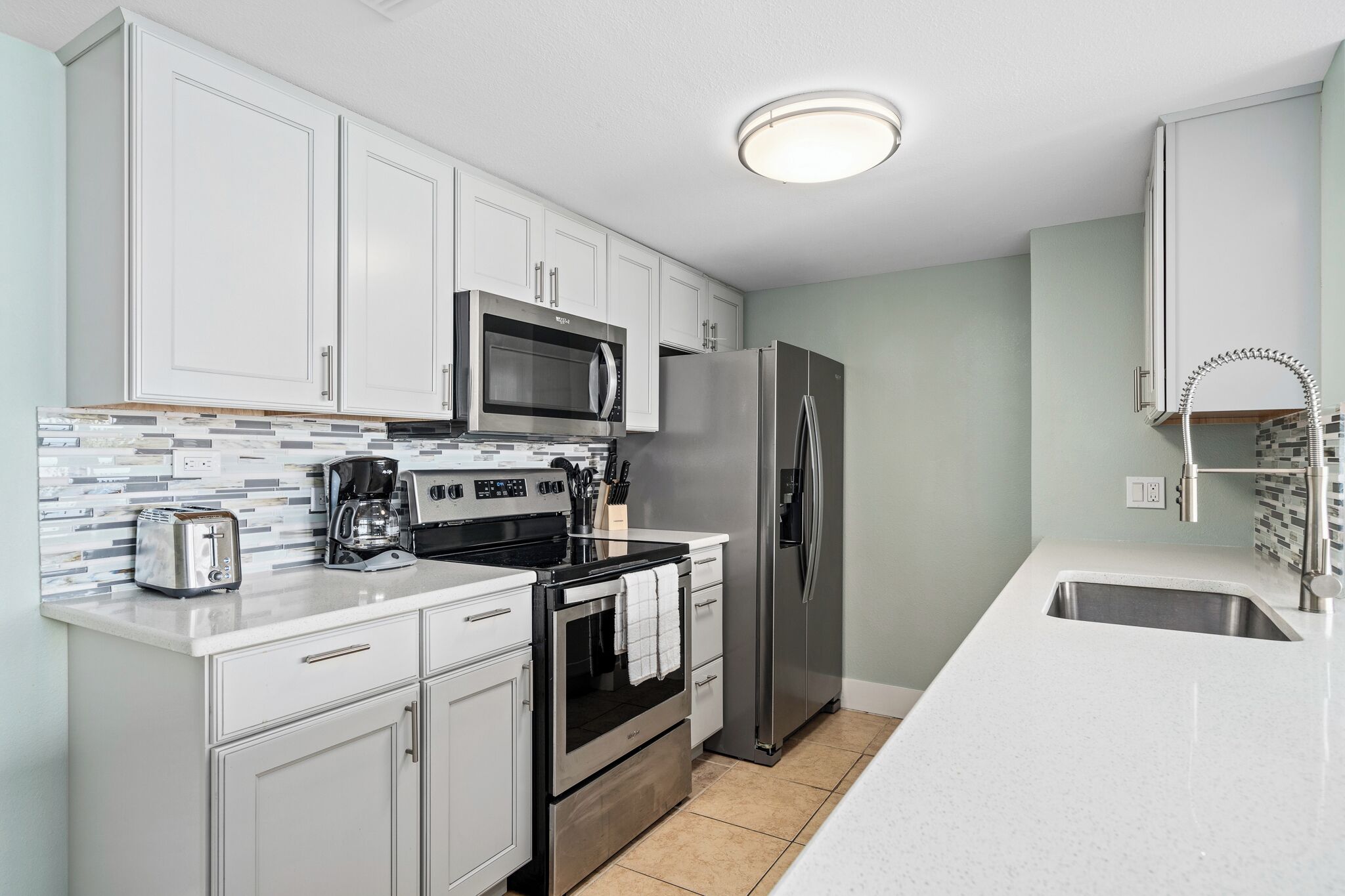A modern kitchen with white cabinets, stainless steel appliances, a tiled backsplash, and a white countertop.