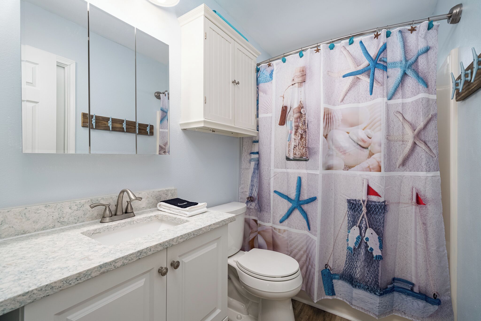 A bathroom with a white vanity, a sink with a faucet, a toilet, and a shower curtain with a starfish design.