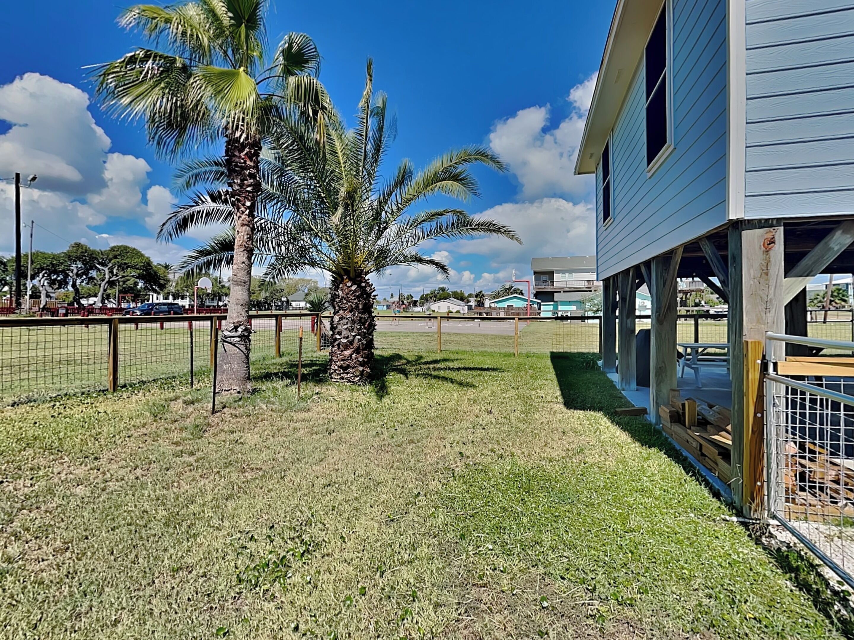 Un barrio residencial con una casa, un patio cercado y una palmera.