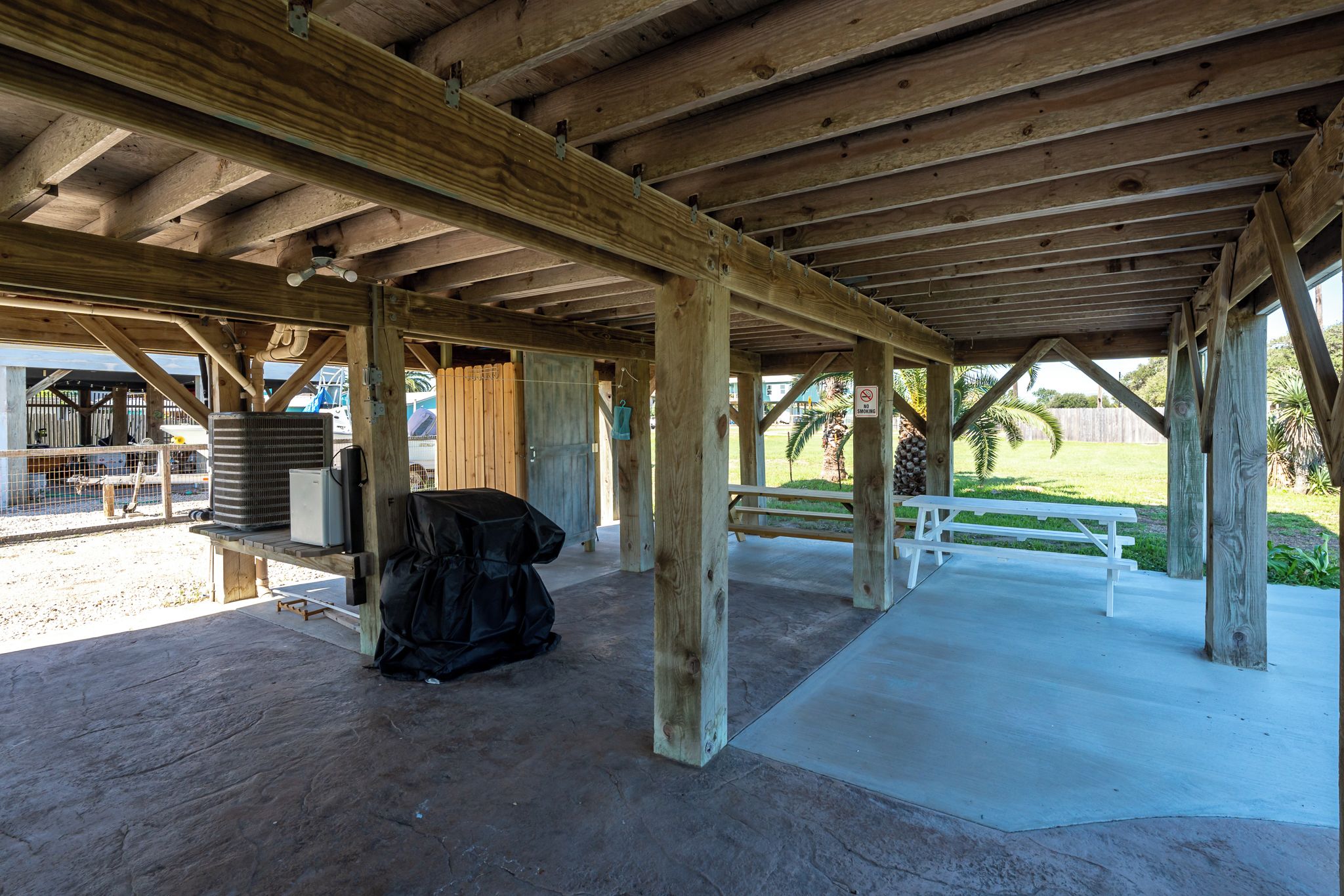 Un espacio al aire libre techado con piso de concreto, vigas de madera y una mesa de picnic.