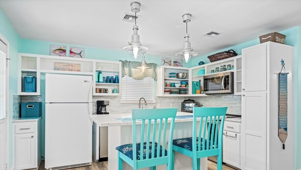 A kitchen with white cabinets, a central island, two turquoise chairs, and pendant lights. - Lunasea Haven by Miss Kitty’s (Rockport)