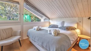 Une chambre avec un grand lit, une chaise, une fenêtre et une vue sur la verdure.