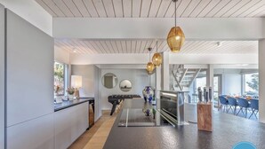 Une cuisine moderne avec un îlot central, un coin repas avec des chaises bleues et une vue sur l’extérieur.