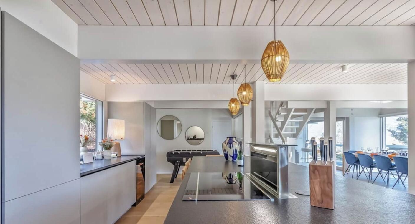 Une cuisine moderne dotée d’un îlot central, de luminaires suspendus et d’un coin repas avec des chaises et une table.