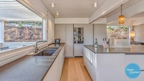 Une cuisine moderne dotée d’une grande fenêtre, d’appareils électroménagers intégrés et offrant une vue sur l’extérieur.