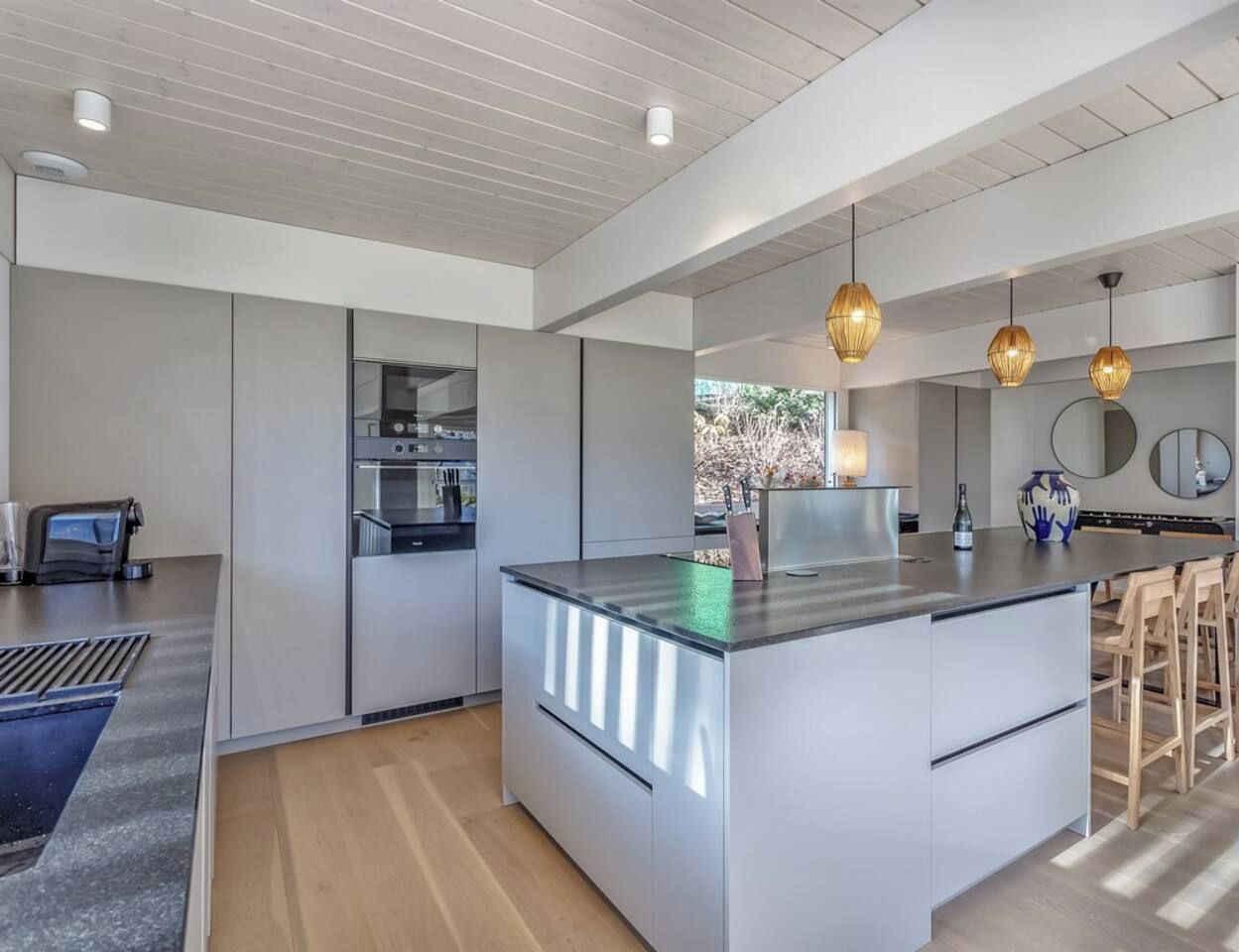 Una cucina moderna con isola centrale, elettrodomestici integrati, illuminazione a sospensione e vista sul paesaggio esterno.