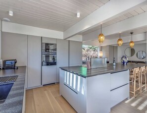 A modern kitchen with a central island, built-in appliances, pendant lighting, and a view of the outdoors.