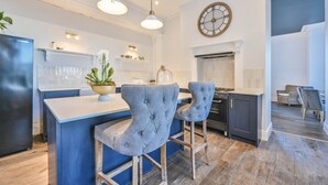 Una cocina moderna con barra, luces colgantes, un reloj y un comedor con sillas.