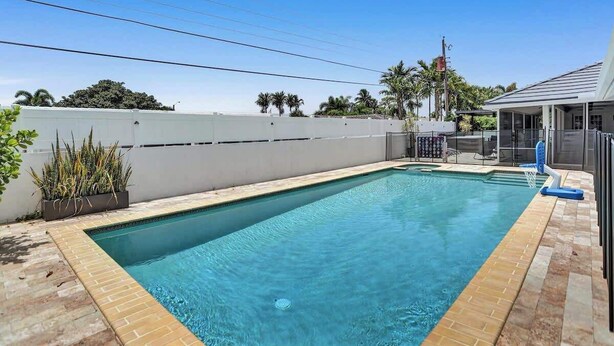 A rectangular swimming pool with a tiled edge, surrounded by a low white wall and a brick patio. - 7BR w/ Heated Pool Jacuzzi, Theatre (Pompano Beach)