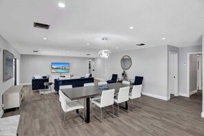 A modern dining area with a large table and chairs, a television, and a decorative mirror. - 7BR w/ Heated Pool Jacuzzi, Theatre (Pompano Beach)