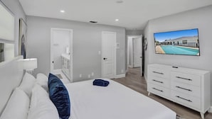 A modern hotel room with a large bed, a TV mounted on the wall, and a view of a swimming pool. - 7BR w/ Heated Pool Jacuzzi, Theatre (Pompano Beach)