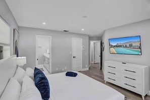 A modern hotel room with a large bed, a TV mounted on the wall, and a view of a swimming pool. - 7BR w/ Heated Pool Jacuzzi, Theatre (Pompano Beach)