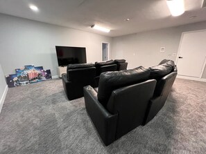 A home theater room with a large flat-screen TV, black leather recliner seating, and a carpeted floor. - 7BR w/ Heated Pool Jacuzzi, Theatre (Pompano Beach)