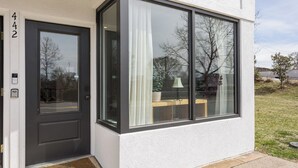 Uma casa moderna com porta frontal escura, uma janela grande com cortinas brancas e o número '442' na parede.