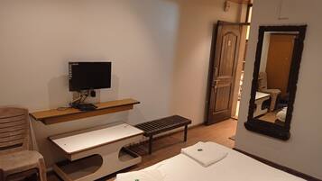 Ein Schlafzimmer mit Bett, Schreibtisch inklusive Computer, Stuhl, Bank und einer Tür.