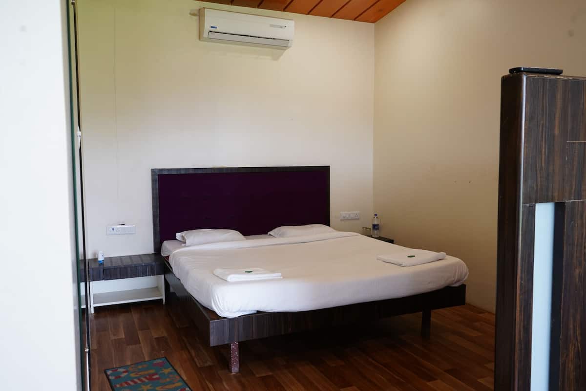 A modern hotel room with a large bed, a wooden floor, a purple headboard, and an air conditioning unit on the wall.