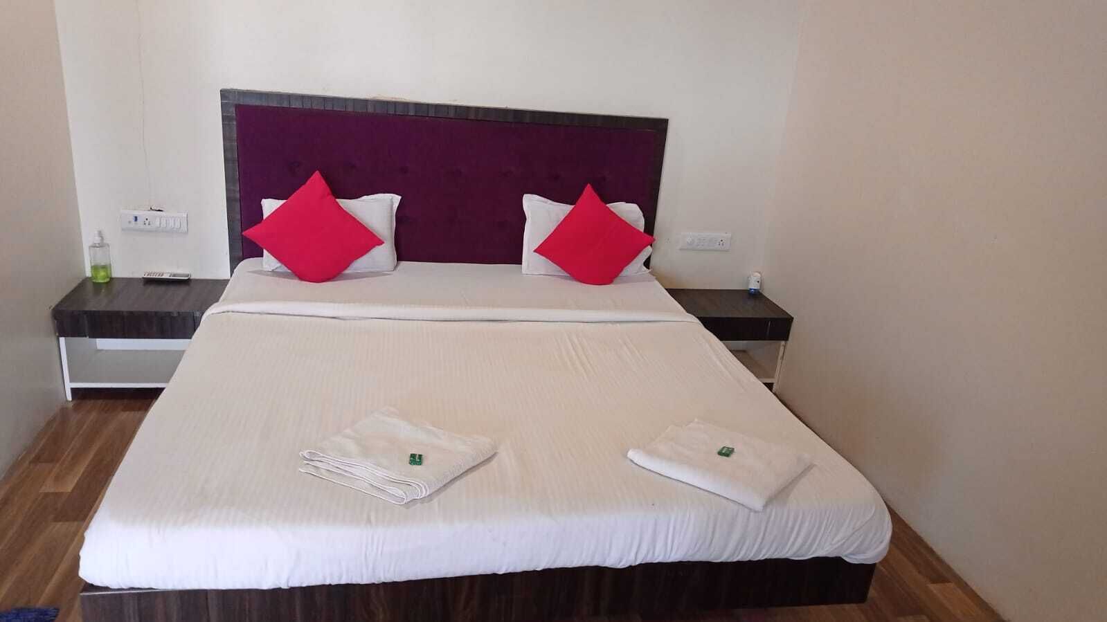 Una cama bien tendida con sábanas blancas, dos almohadas rojas y dos toallas dobladas sobre la cama.