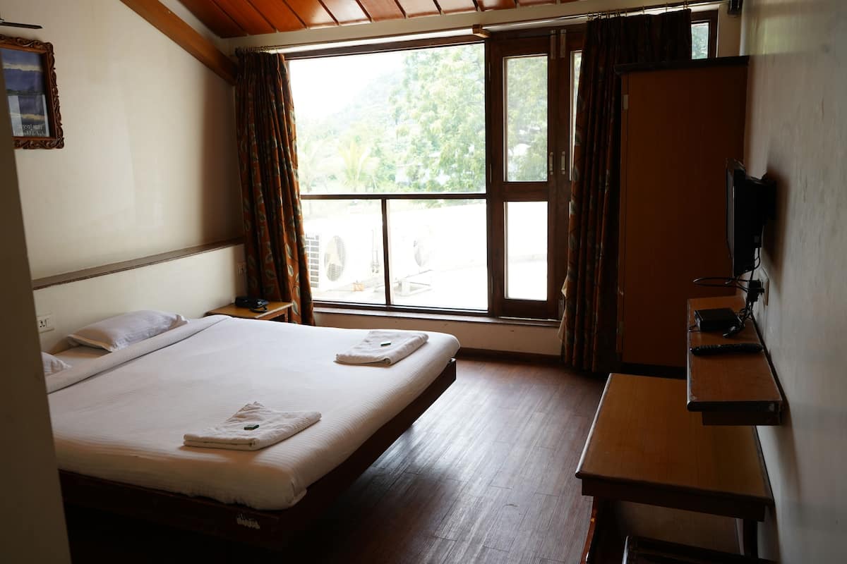 A hotel room with a bed, a desk, a TV, and a window with curtains.