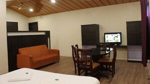 A room with a bed, an orange sofa, a dining table with chairs, a television, and wooden cabinets. - Lotus Resort (Chhatrapati Sambhajinagar)