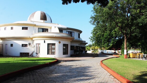 A white building with a dome and circular design, paved walkway, and green lawn. - Lotus Resort (Chhatrapati Sambhajinagar)